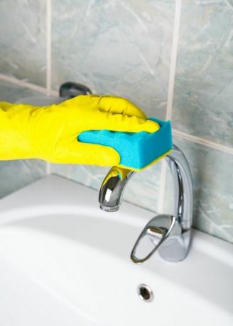 pandemian desinfiointi mies keltaisissa käsineissä puhdistaa kylpyhuonehanan ja kylpy- ja pesuallas siivooja keltaisissa suojakäsineissä pesee likaisen kylpyammeen tai pesualtaan miehen kädet pesee tai puhdistaa kylpy läheltä