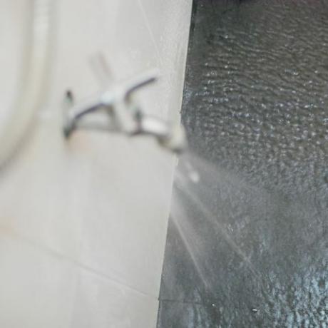 vuotaa vettä hanasta, joka roiskuu kylpyhuoneen lattiaan korkean vedenpaineen takia