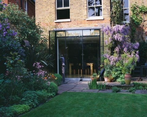 Näkymä nurmikolta ja talon takaa, jossa on suorakulmainen uima-allas, wisteria, lasinen keittiö ja Helen Sinclairin veistos