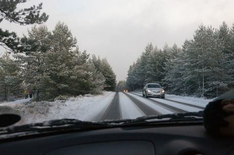 Auto ajaa lumen peittämällä tiellä puiden keskuudessa