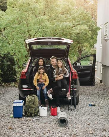 hymyilevät vanhemmat istuvat tyttärien kanssa sähköauton tavaratilassa