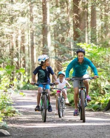 nainen ja hänen kaksi lastaan ​​ajavat pyörällä metsässä auringonpaisteessa