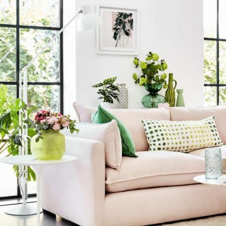 vaaleanpunainen sohva valkoisessa huoneessa vihreiden kasvien ympärillä ja vihreillä kuvioiduilla tyynyillä