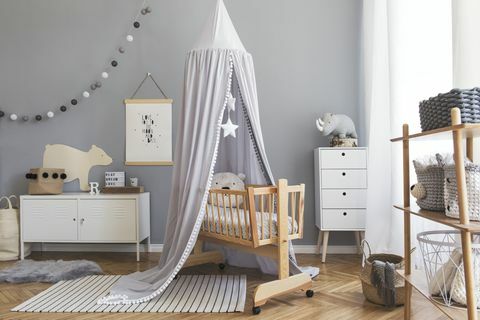 Tyylikäs skandinaavisen vastasyntyneen vauvan huoneen sisustus, jossa on juliste, valkoiset huonekalut, luonnolliset lelut, harmaa katos, jossa tähdet ja nallekarhut. Minimalistinen ja viihtyisä sisustus lastenhuoneessa.