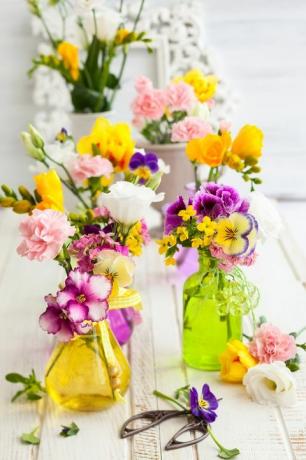 Kauniit tuoreet kukat lasipulloissa puupöydällä