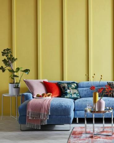valoisa olohuone, jossa keltainen paneloitu seinä ja sininen sohva