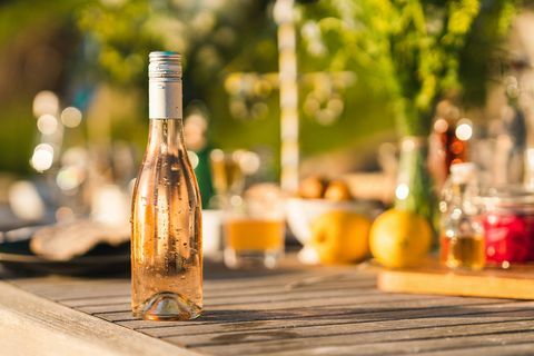 avaamaton pullo kylmää ruusuviiniä juhannuksen ruokapöydällä ruotsissa keskittyen etualalla tippuvaan tuoreeseen pulloon