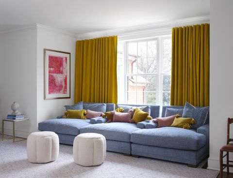sininen sohva, keltaiset verhot, vaaleanpunaiset ja keltaiset tyynyt