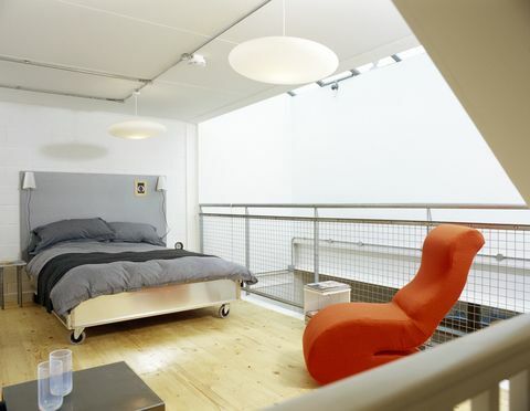 Moderni makuuhuone harmaalla peitolla ja kirkkaan oranssilla tuolilla