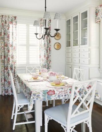 aamiaishuone, valkoiset ruokapöydän tuolit, valkoiset ja siniset riisutut tuolityynyt, valkoinen säilytystila, kukkaverhot ja pöytälevy