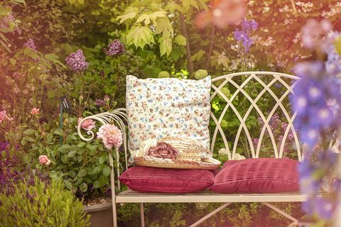 Kaunis kesäinen valurautainen puutarhatuoli, jossa tyynyt ja kesähattu, nuhjuinen tyylikäs kohtaus